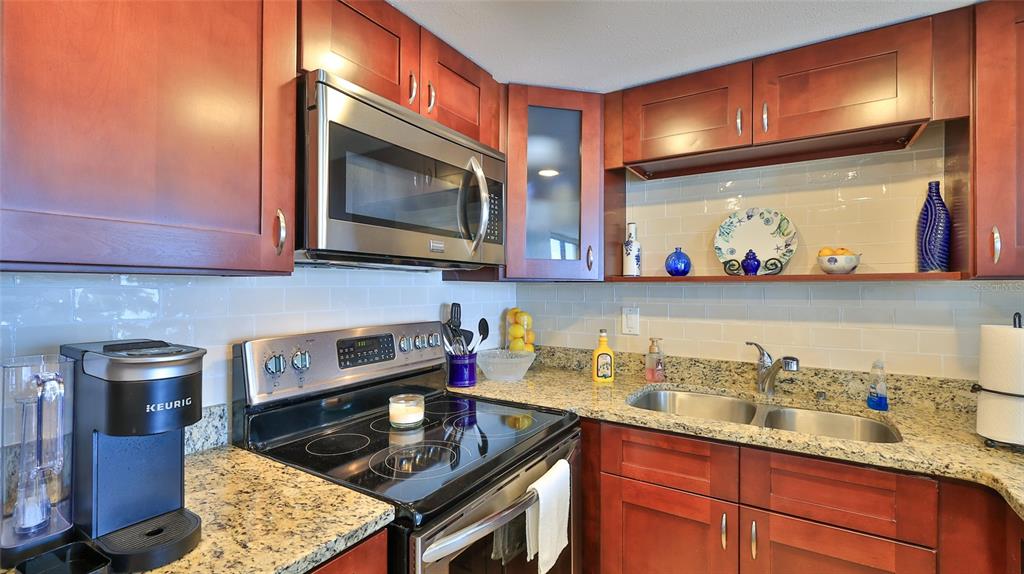 A kitchen features cherry wood cabinets, granite countertops, stainless steel appliances, and a subway tile backsplash — 3051 S ATLANTIC AVENUE UNIT 2206, DAYTONA BEACH, FL