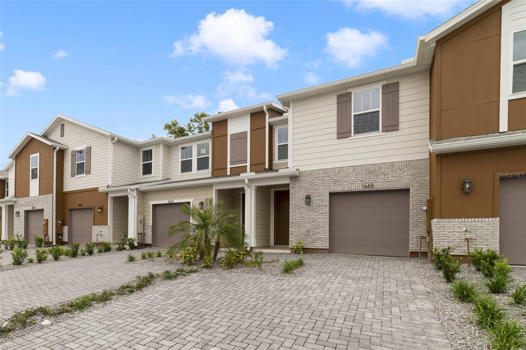 A row of modern townhomes features tan siding, brick accents, and paved driveways under a sky — 1665 GREENLEAF WOODS COVE, OVIEDO, FL