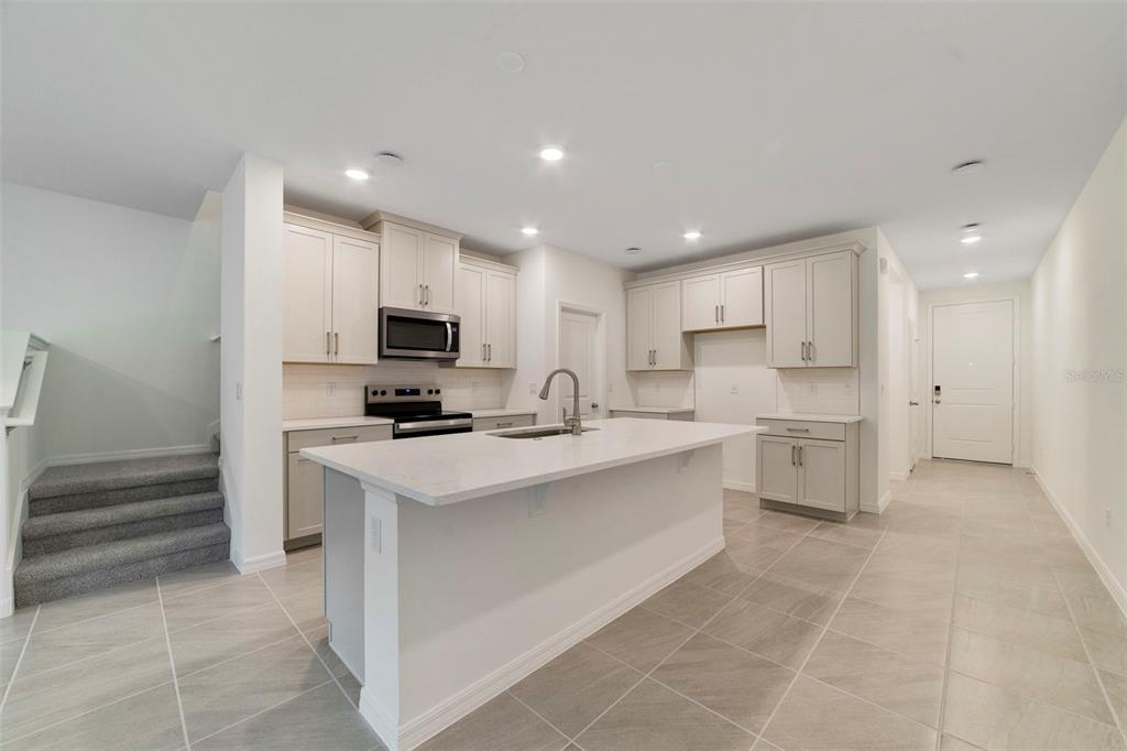 A modern kitchen features light-colored cabinetry, a central island with a sink, and tile flooring — 1665 GREENLEAF WOODS COVE, OVIEDO, FL