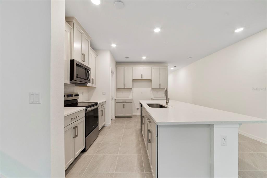 A modern kitchen features light gray cabinets, stainless steel appliances, and a large central island — 1665 GREENLEAF WOODS COVE, OVIEDO, FL