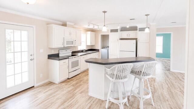 A kitchen with white cabinets, dark countertops, a breakfast bar, and light wood flooring — 7079 SE Bluebird Circle, Hobe Sound FL 33455, HOBE SOUND, FL