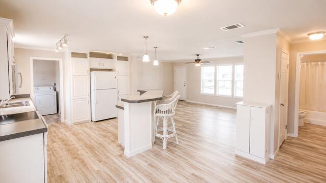 A kitchen with white cabinets, a breakfast bar, and light wood-look flooring — 7079 SE Bluebird Circle, Hobe Sound FL 33455, HOBE SOUND, FL