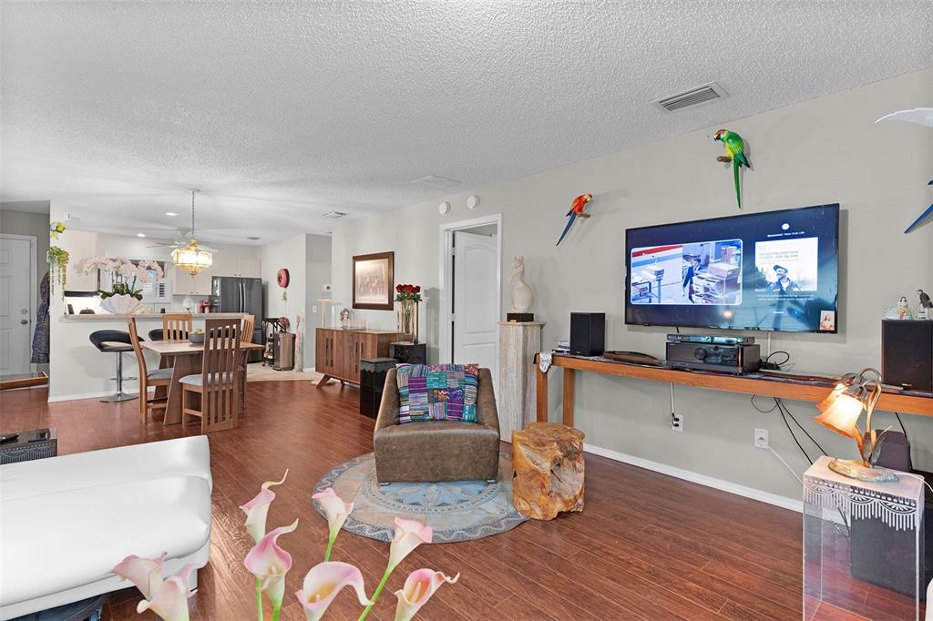 A living room with wood-look flooring, a wall-mounted television, and an adjacent dining area — 7851 SE 173RD PANORAMA PLACE, THE VILLAGES, FL