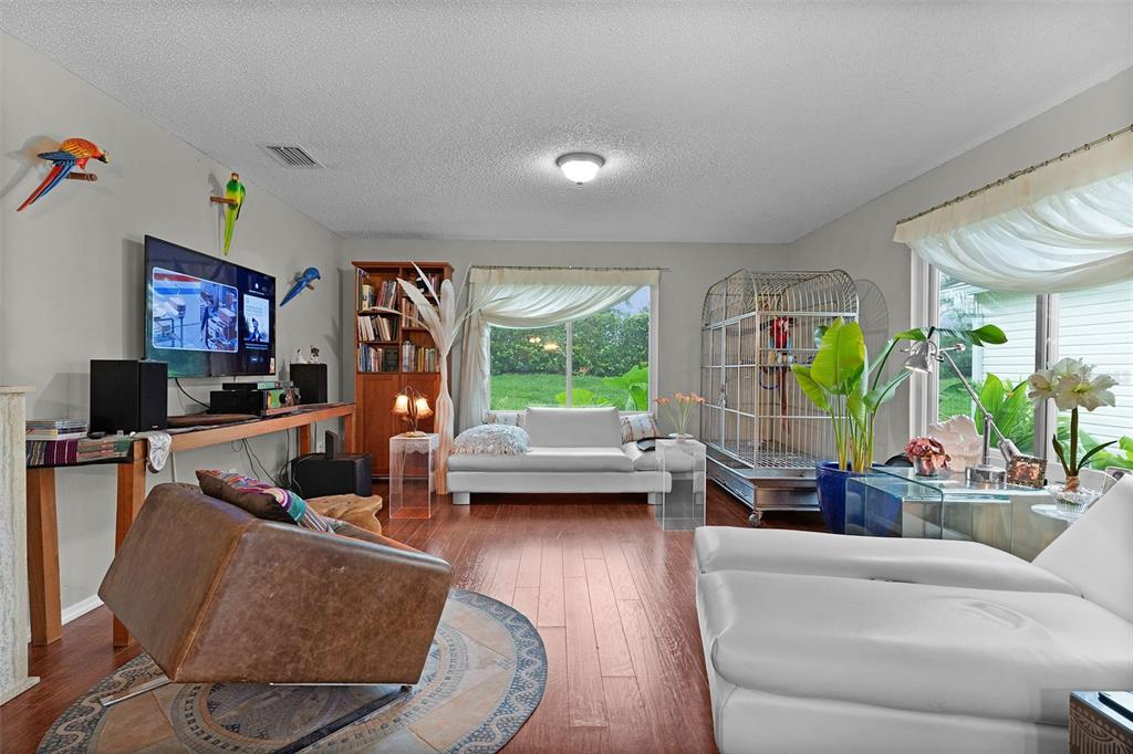 A living room features wood flooring, white sofas, a large birdcage, and a television — 7851 SE 173RD PANORAMA PLACE, THE VILLAGES, FL