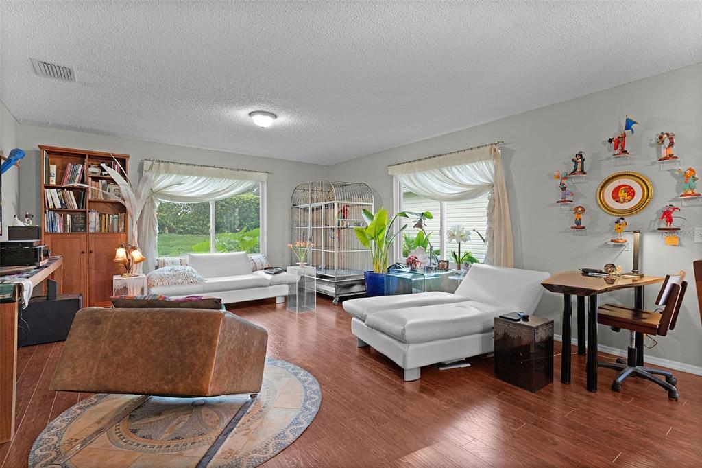 A living room with wood flooring, white furniture, a large birdcage, and wall-mounted decorative figures — 7851 SE 173RD PANORAMA PLACE, THE VILLAGES, FL