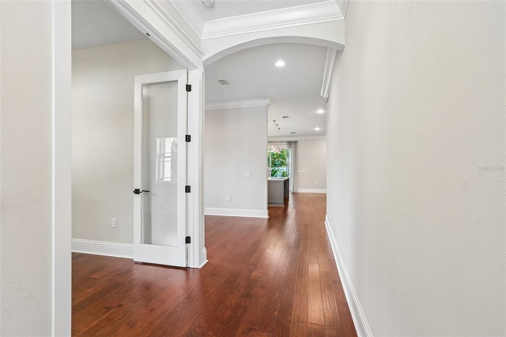A hallway with hardwood floors leads to an open-concept kitchen with a glass-paneled door — 3627 E CLARK CIRCLE, TAMPA, FL