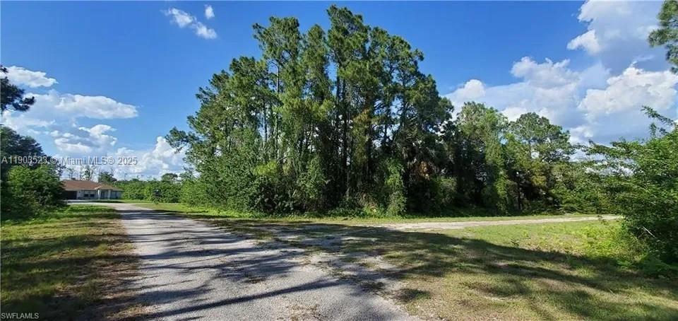 A gravel road leads toward a wooded lot with a house visible in the distance — 676 KODAK ST, Lehigh Acres FL 33972, LEHIGH ACRES, FL