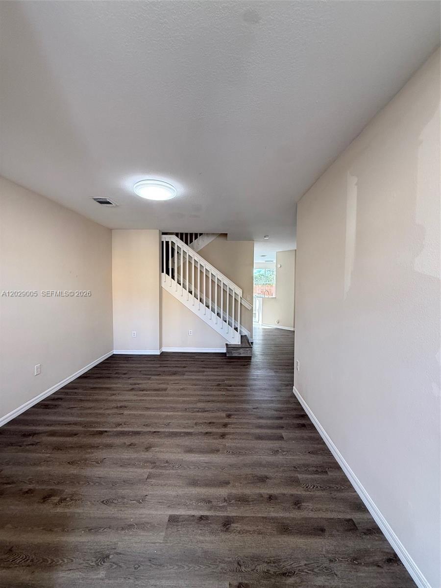 An empty room features dark wood-look flooring, light-colored walls, and a white staircase — 8528 SW 166th Pl # 8528, Miami FL 33193, MIAMI, FL