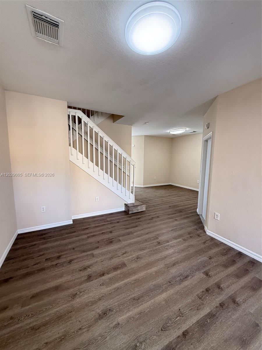 An empty room features wood-look flooring, a white staircase with a railing, and beige walls — 8528 SW 166th Pl # 8528, Miami FL 33193, MIAMI, FL