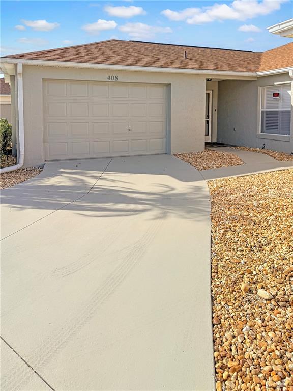 A beige house exterior features a single-car garage, a concrete driveway, and gravel landscaping — 408 DUARTE LANE, THE VILLAGES, FL