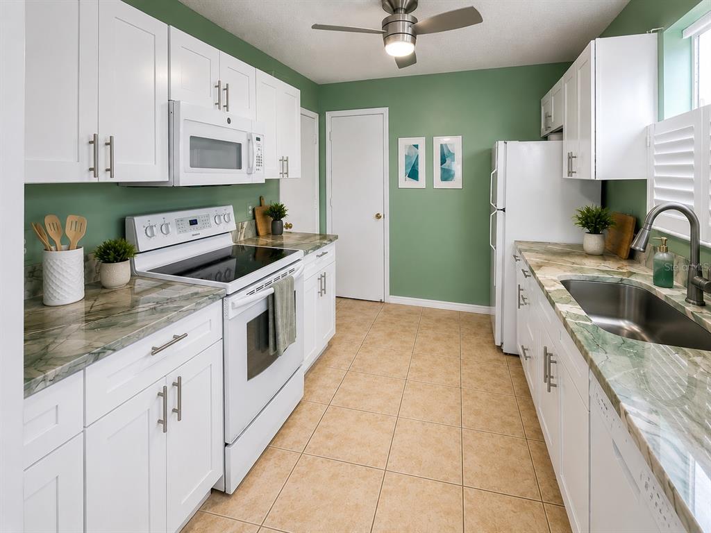 A kitchen with white cabinets, green walls, stone countertops, and stainless steel appliances — 408 DUARTE LANE, THE VILLAGES, FL