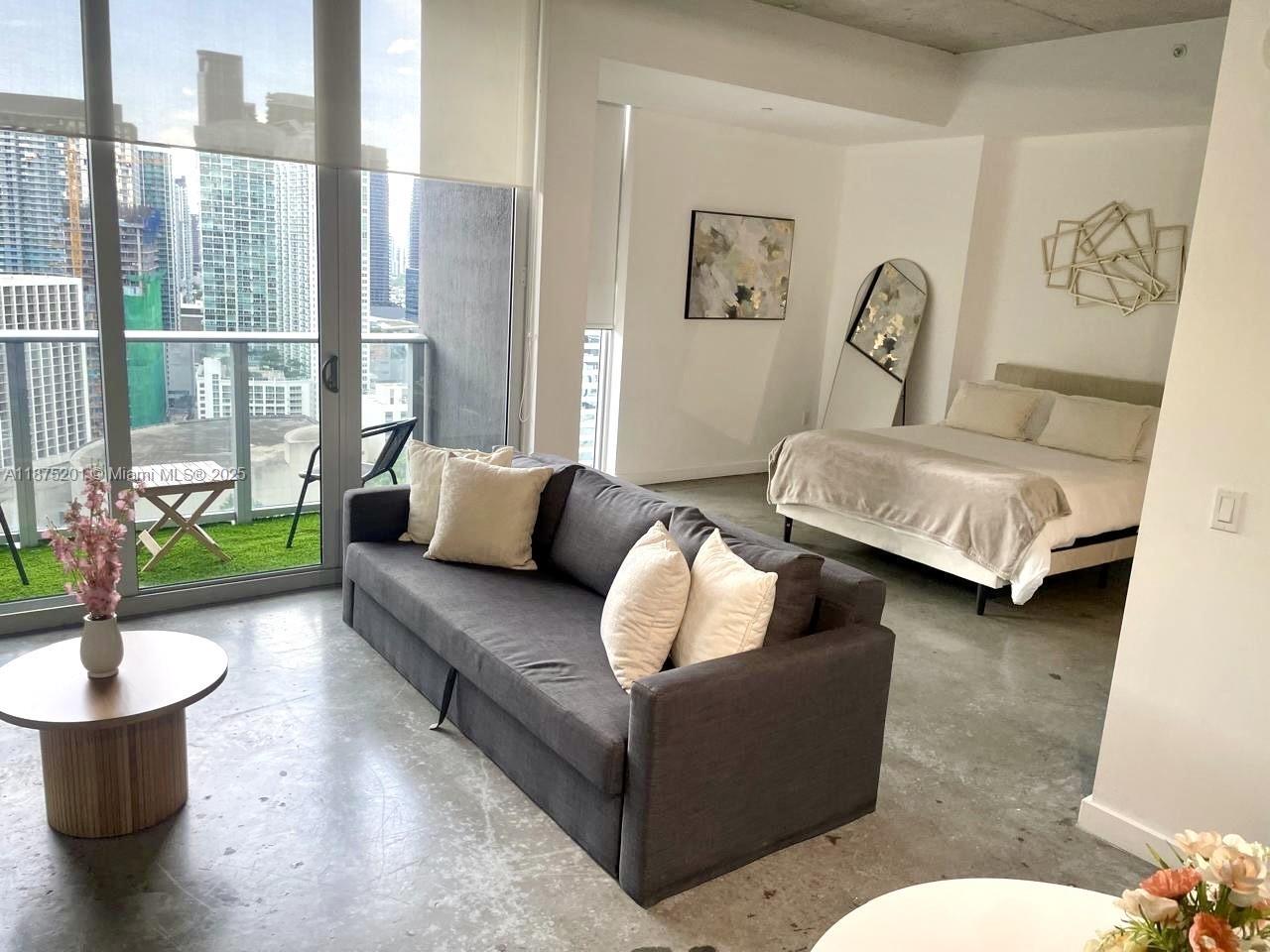 A studio apartment features a gray sofa, a bed, and a balcony with city views — 151 SE 1st St # 2807, Miami FL 33131, MIAMI, FL