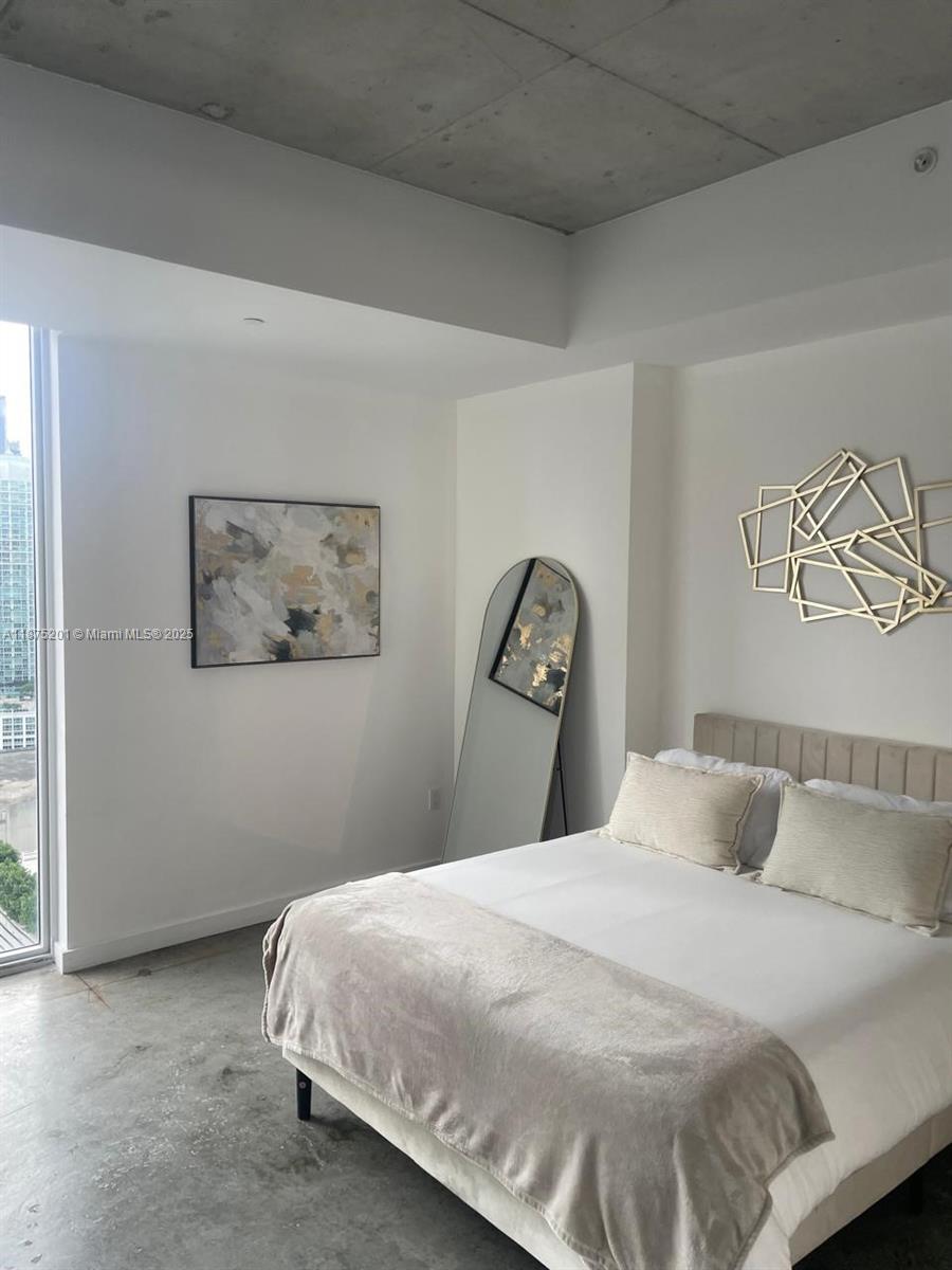 A bedroom features a bed, a floor mirror, wall art, and a concrete ceiling — 151 SE 1st St # 2807, Miami FL 33131, MIAMI, FL