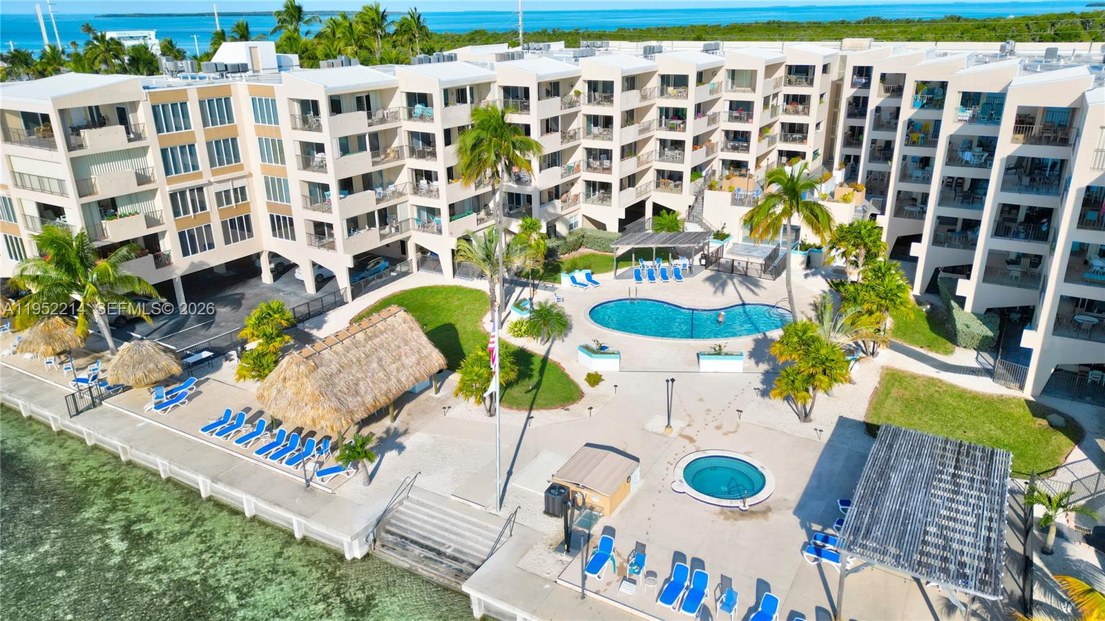 An aerial view shows a multi-story apartment complex with a pool, hot tub, and tiki hut — 79901 Overseas Higway # 204, Islamorada FL 33036, ISLAMORADA, FL