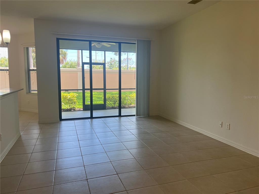An empty living area with beige tile flooring, a sliding glass door, and a screened patio — 1498 MASENO DRIVE, VENICE, FL