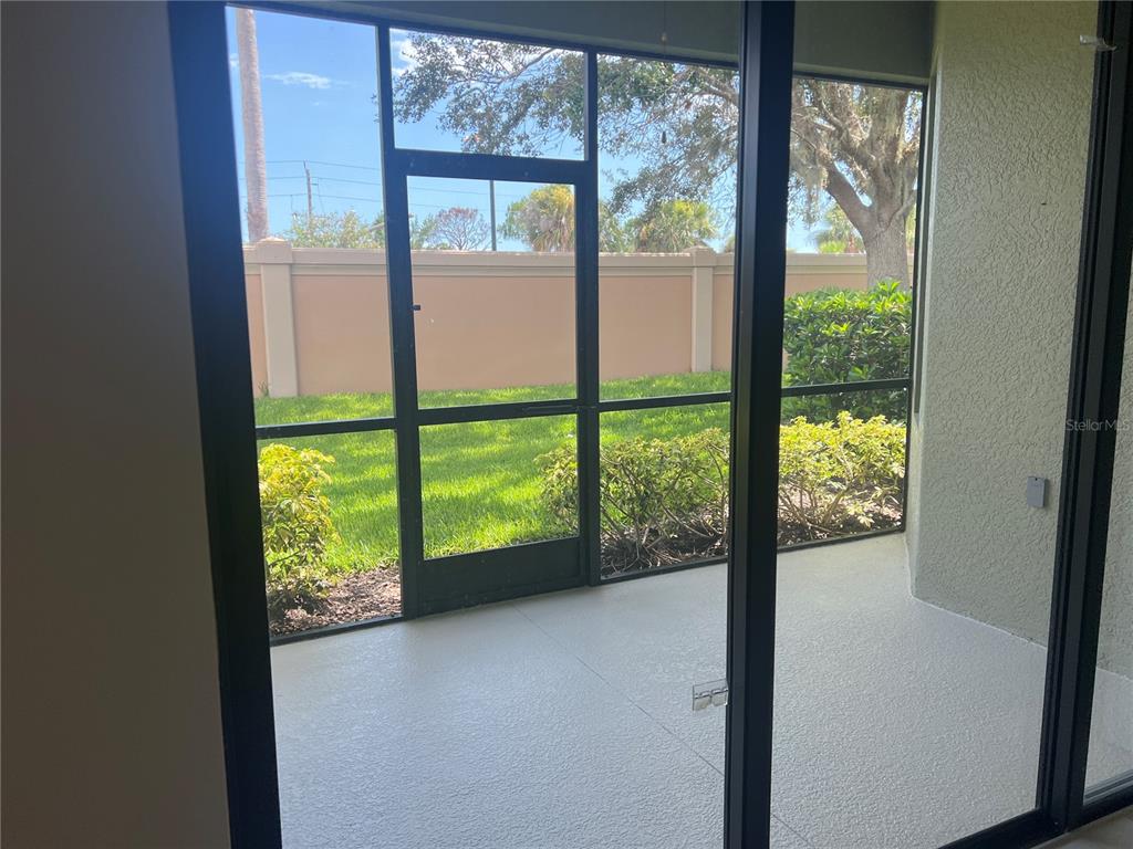 A screened-in patio with a concrete floor overlooks a grassy yard and a perimeter wall — 1498 MASENO DRIVE, VENICE, FL