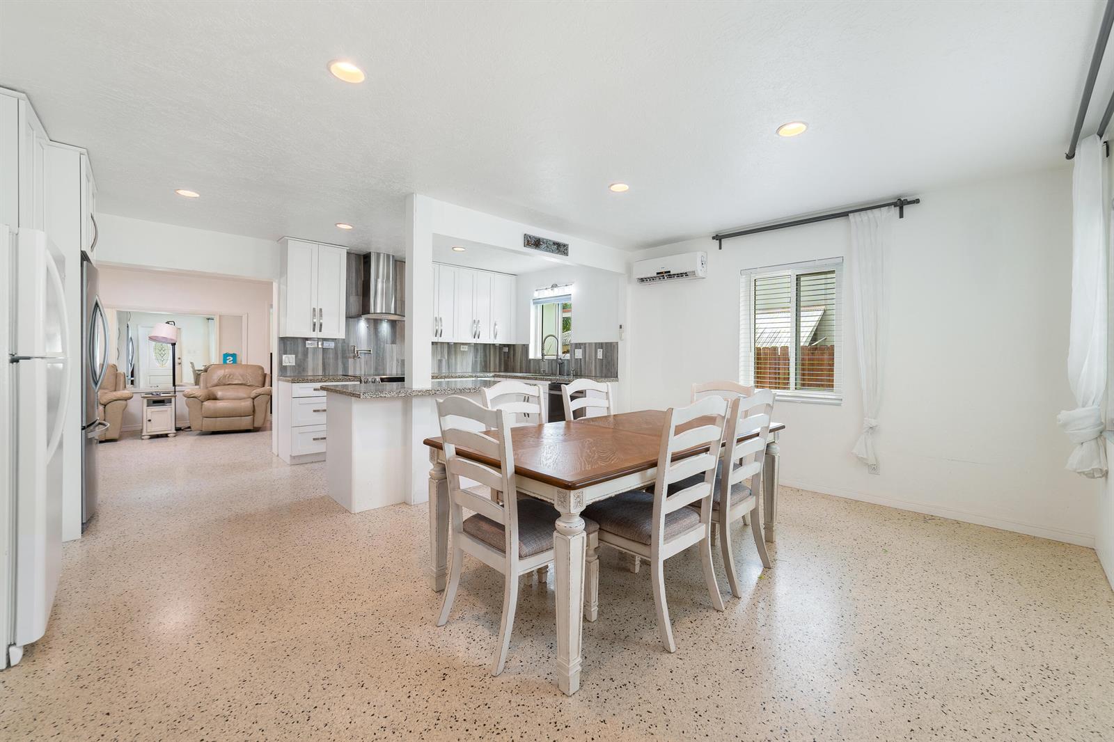 A dining area with a wooden table and white chairs sits adjacent to a kitchen — 245 SW 5th Street, Dania Beach FL 33004, DANIA BEACH, FL