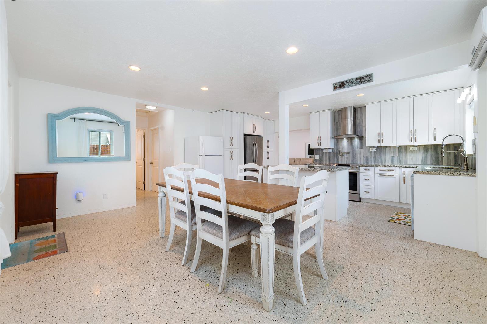 A dining area with a wooden table and white chairs sits adjacent to a modern kitchen — 245 SW 5th Street, Dania Beach FL 33004, DANIA BEACH, FL