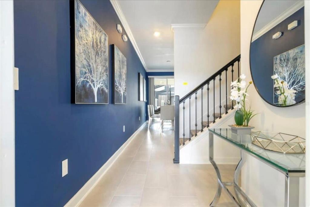 A hallway with a blue accent wall, tiled floor, staircase, and a glass console table — 2709 SCRAPBOOK STREET, KISSIMMEE, FL