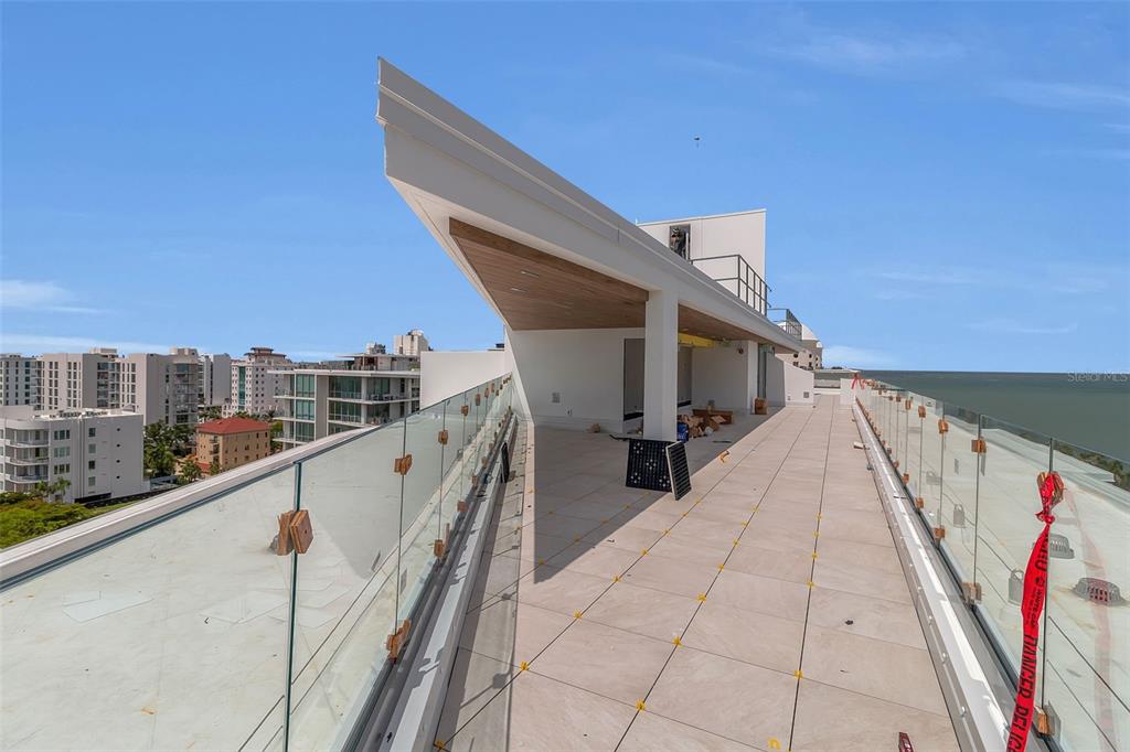 A high-rise balcony with glass railings, light-colored tile flooring, and a modern architectural overhang — 688 GOLDEN GATE POINT UNIT 801, SARASOTA, FL