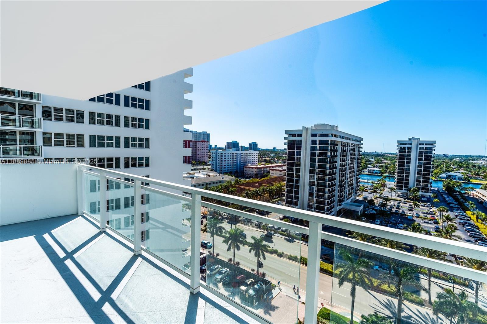 A balcony with a glass railing overlooks a city street, parking lot, and tall buildings — 2030 S Ocean Dr # 1127, Hallandale Beach FL 33009, HALLANDALE BEACH, FL