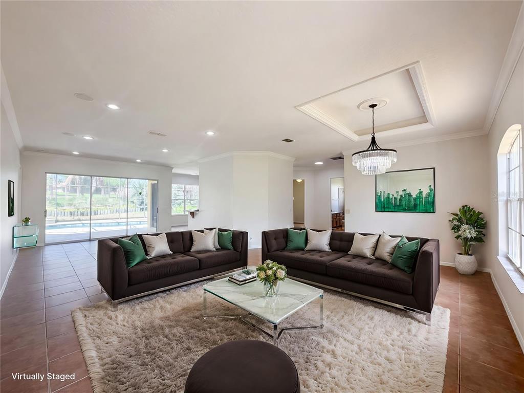 A living room with two dark sofas, a glass coffee table, and a large chandelier — 10408 LAGO LOUISA COURT, CLERMONT, FL