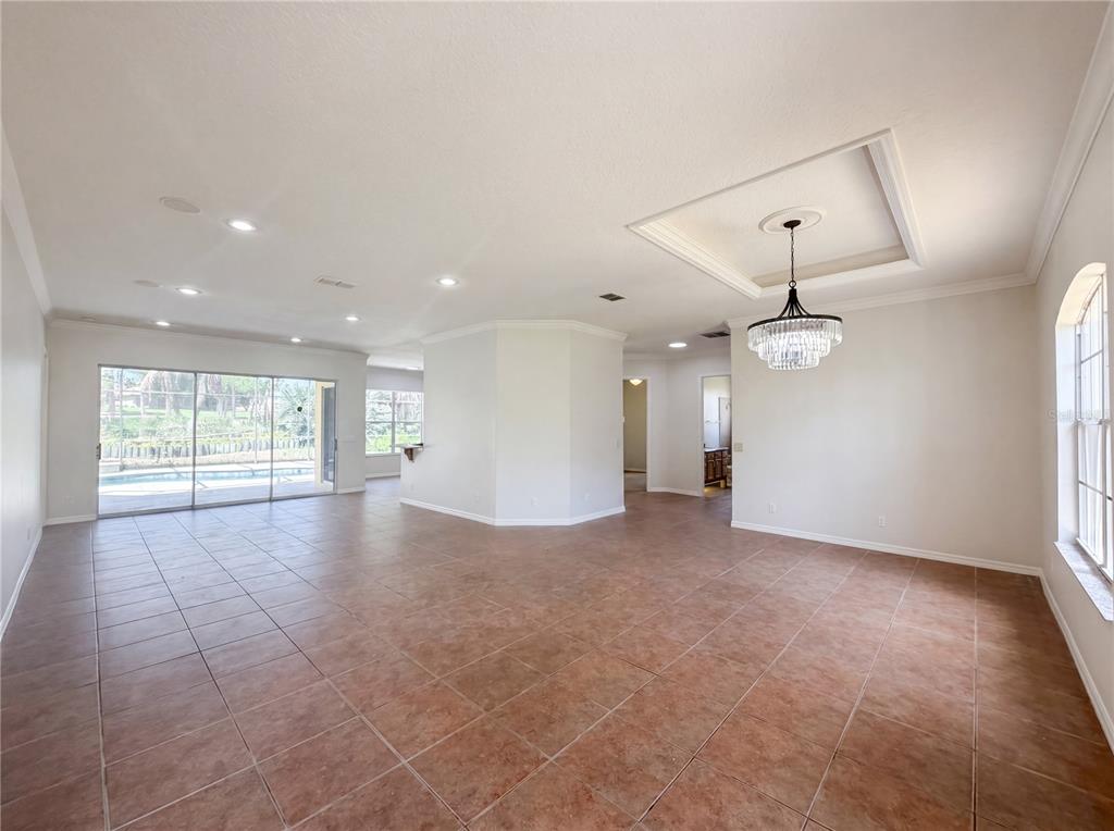 An open-concept living area features tile flooring, a tray ceiling with a chandelier, and sliding doors — 10408 LAGO LOUISA COURT, CLERMONT, FL