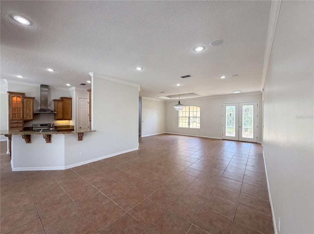 An open-concept kitchen with wood cabinets and a breakfast bar overlooks a tiled living area — 10408 LAGO LOUISA COURT, CLERMONT, FL