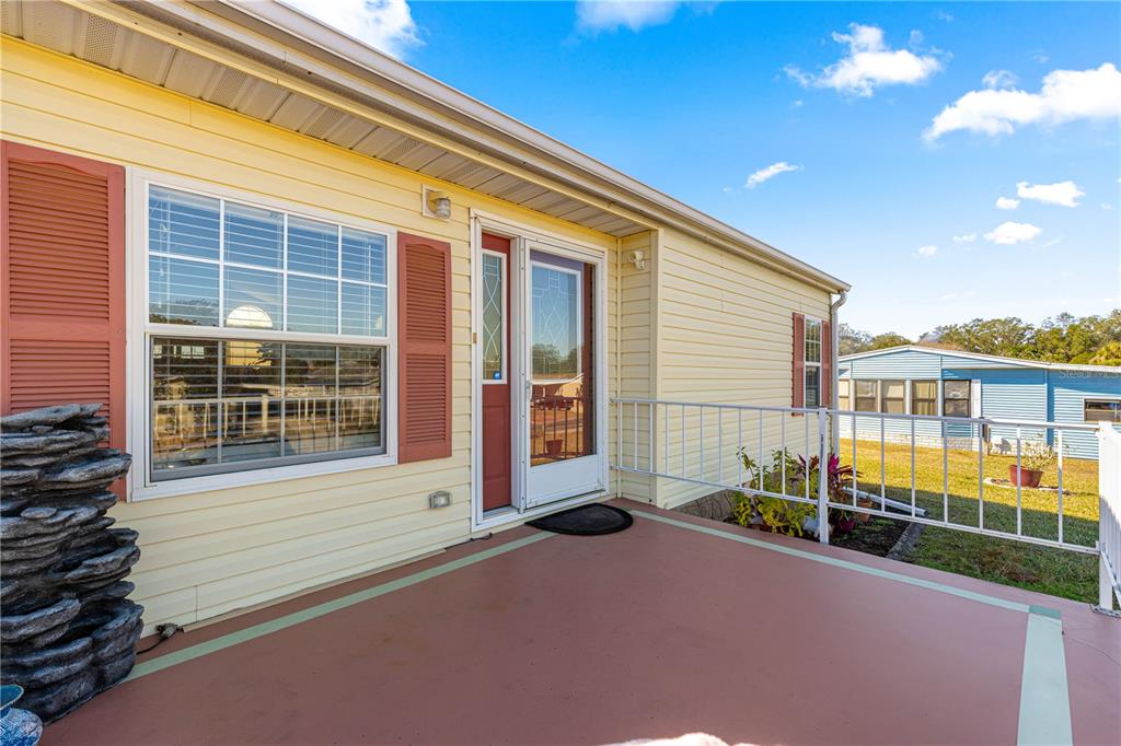 A yellow house exterior features a covered patio, a white railing, and a glass door — 9630 SE 165TH LANE, SUMMERFIELD, FL