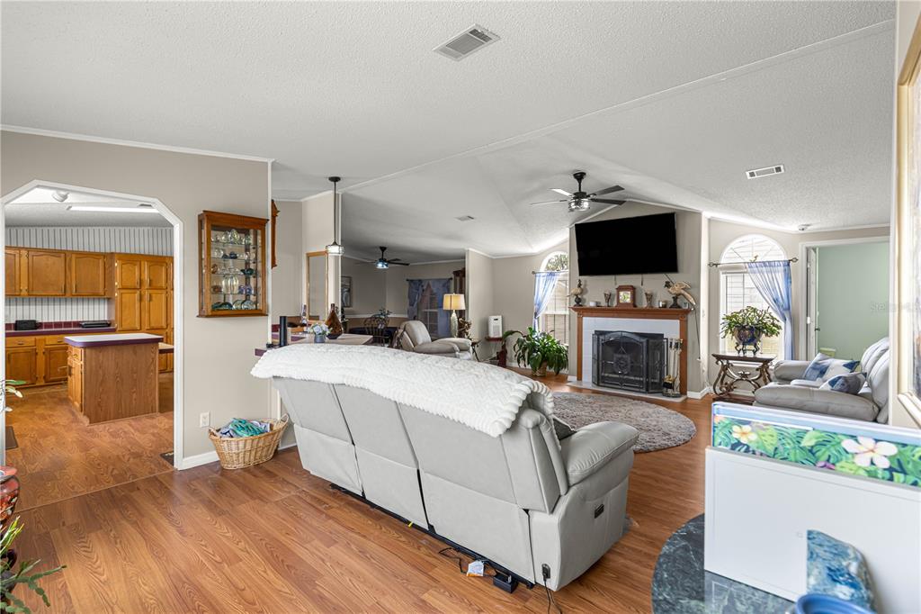 A living room with a fireplace, vaulted ceiling, and an adjacent kitchen with wood cabinets — 9630 SE 165TH LANE, SUMMERFIELD, FL