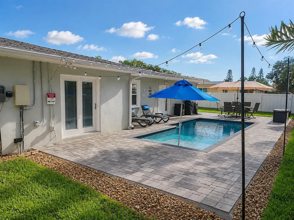 A backyard patio features a swimming pool, a blue umbrella, lounge chairs, and string lights — 2001 MAGNOLIA DRIVE, CLEARWATER, FL