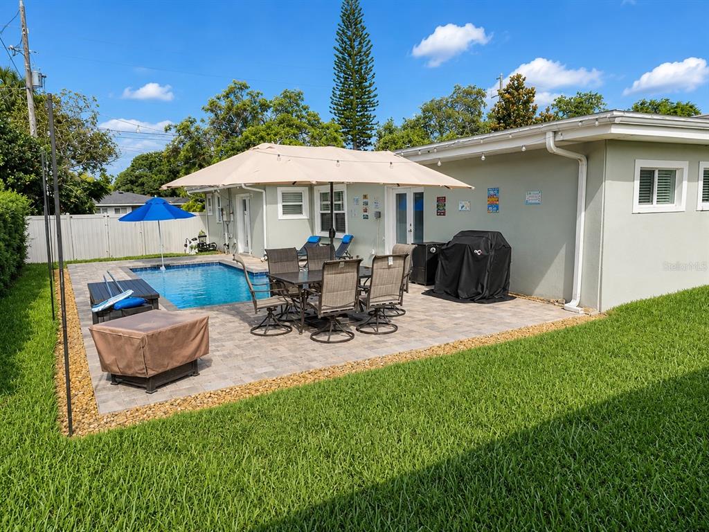 A backyard patio features a swimming pool, outdoor dining set, umbrella, and a covered grill — 2001 MAGNOLIA DRIVE, CLEARWATER, FL