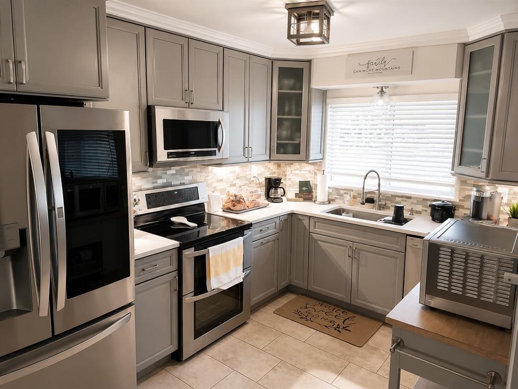 A kitchen features gray cabinets, stainless steel appliances, a tile backsplash, and a window above the sink — 2001 MAGNOLIA DRIVE, CLEARWATER, FL
