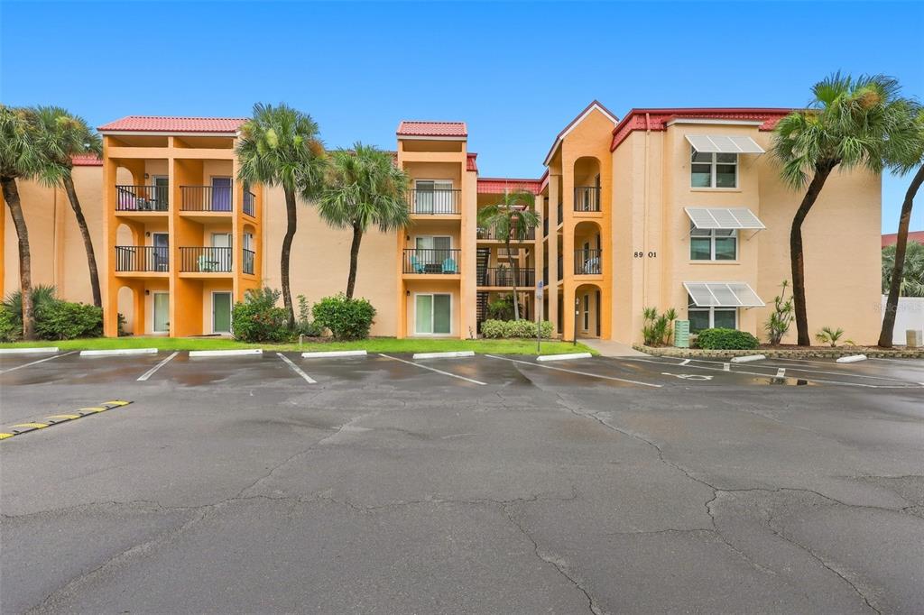 A three-story apartment building with a tan stucco exterior, orange accents, and palm trees — 8901 BLIND PASS ROAD UNIT 232, ST PETE BEACH, FL