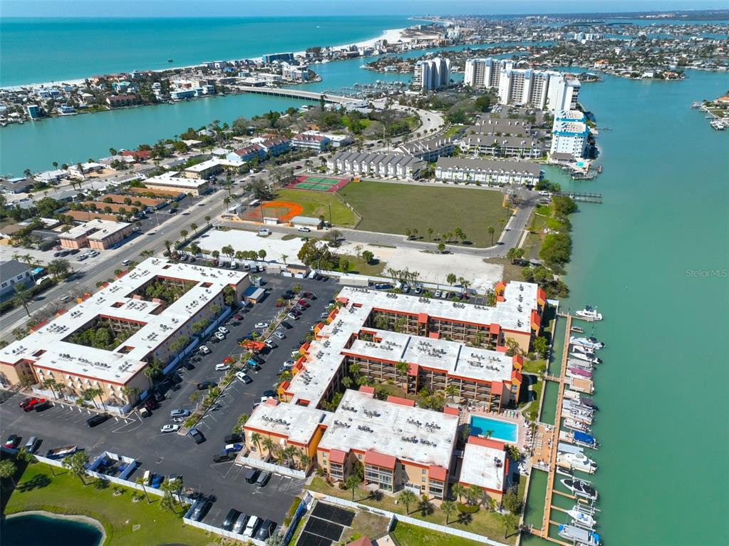 An aerial view shows waterfront condominium buildings with a parking lot, pool, and boat slips — 8901 BLIND PASS ROAD UNIT 232, ST PETE BEACH, FL