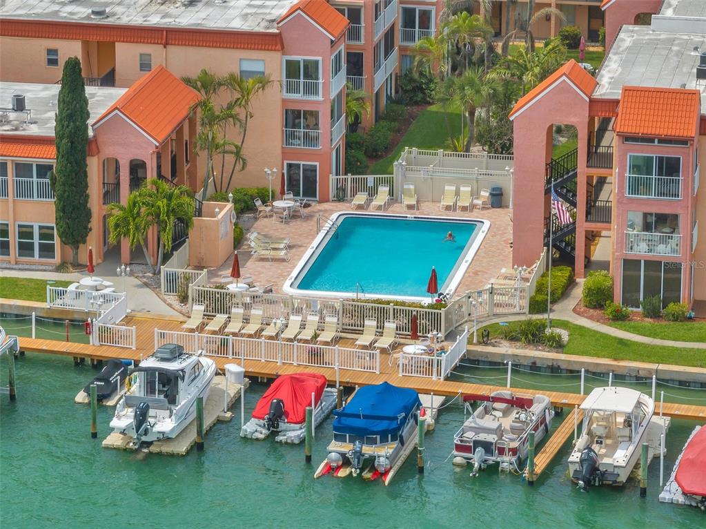 An aerial view shows a swimming pool and boat docks at a waterfront apartment complex — 8901 BLIND PASS ROAD UNIT 232, ST PETE BEACH, FL