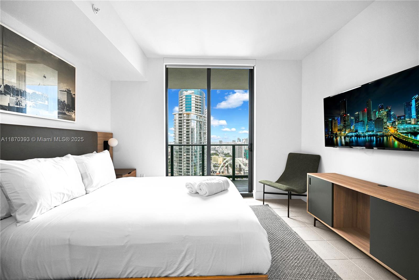 A modern bedroom features a bed, a wall-mounted television, and a balcony with city views — 159 NE 6th St # 3901, Miami FL 33132, MIAMI, FL