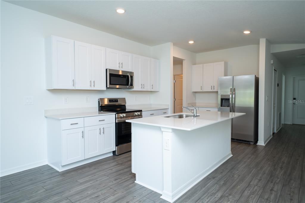A kitchen features white cabinets, stainless steel appliances, a center island, and gray wood flooring — 1481 NW 48TH TER, OCALA, FL