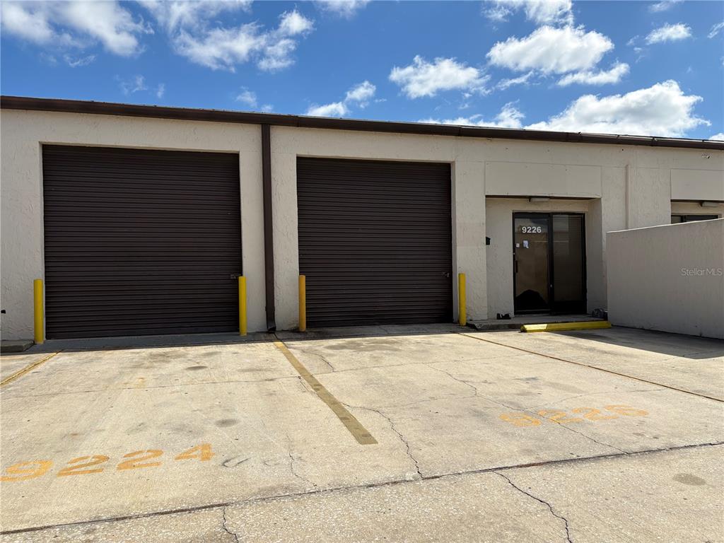 An exterior view of a commercial building featuring two roll-up doors and a glass entrance — 9212 LAZY LANE, TAMPA, FL