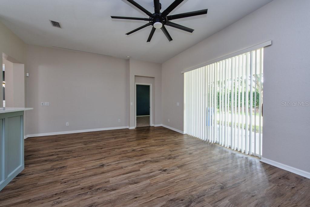 An empty room features wood-look flooring, a ceiling fan, and vertical blinds over sliding doors — 11104 HOLLY CONE DRIVE, RIVERVIEW, FL