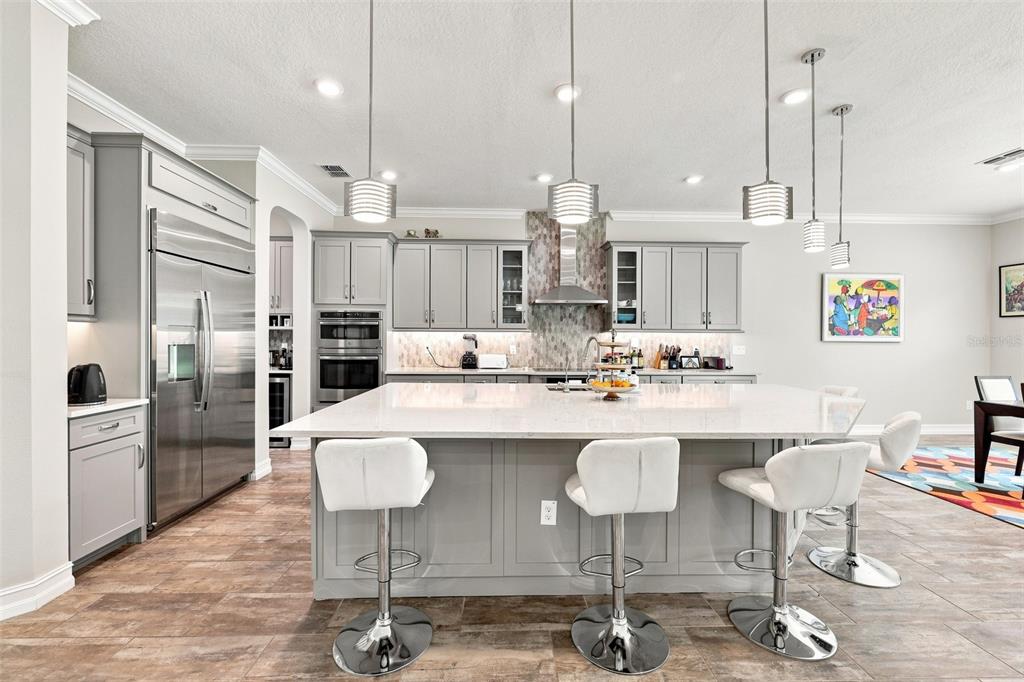 A modern kitchen features gray cabinetry, a large white island with barstools, and stainless appliances — 3225 CORDOBA RANCH BOULEVARD, LUTZ, FL