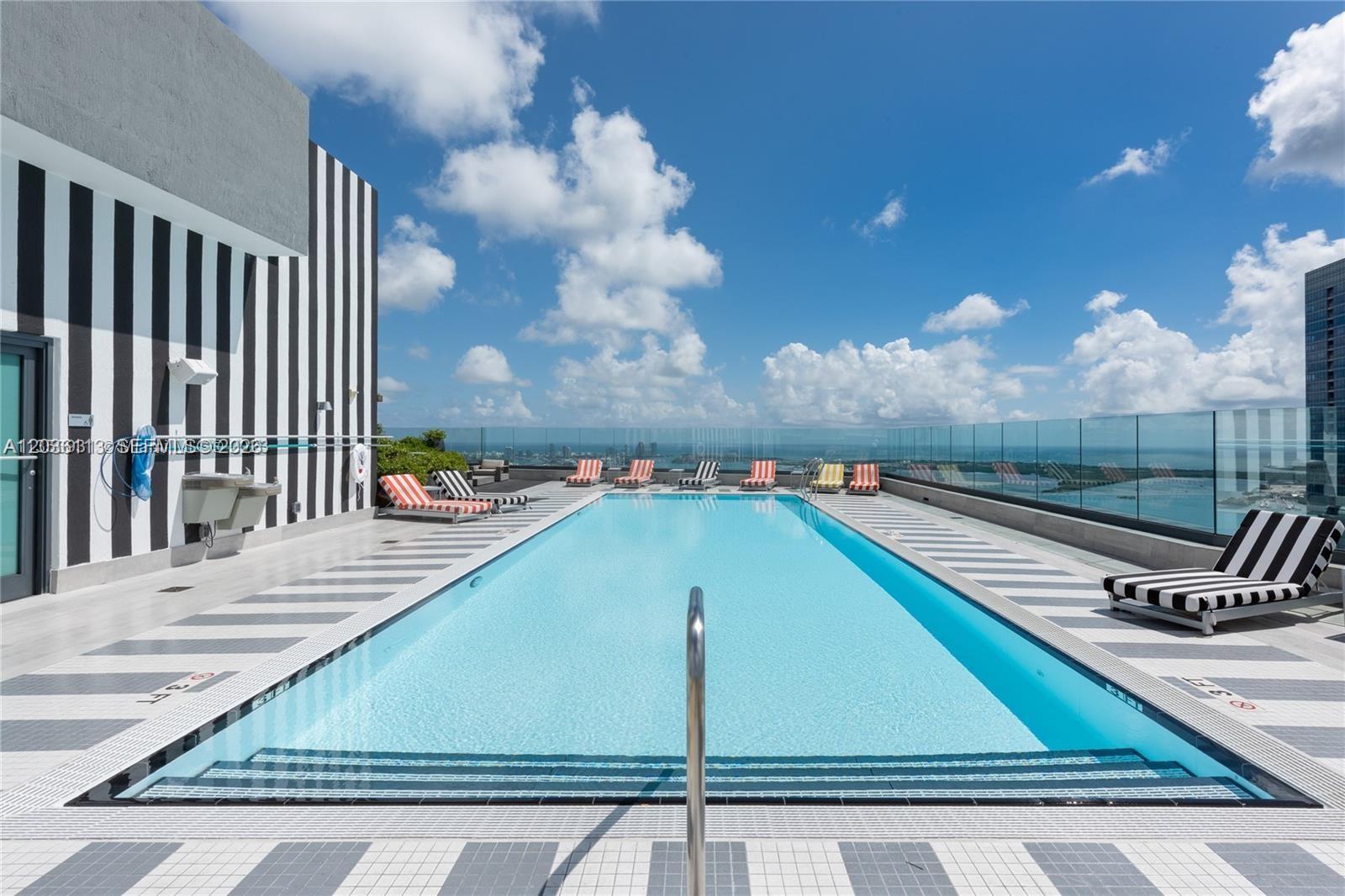 A rooftop swimming pool features striped lounge chairs and a glass railing overlooking the city — 1300 S Miami Ave # 1103, Miami FL 33130, MIAMI, FL