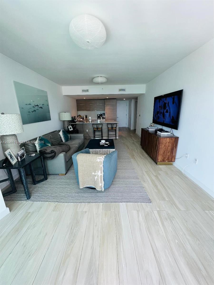 This living room features light wood flooring, a grey sofa, and an open kitchen area — 1300 S Miami Ave # 1103, Miami FL 33130, MIAMI, FL