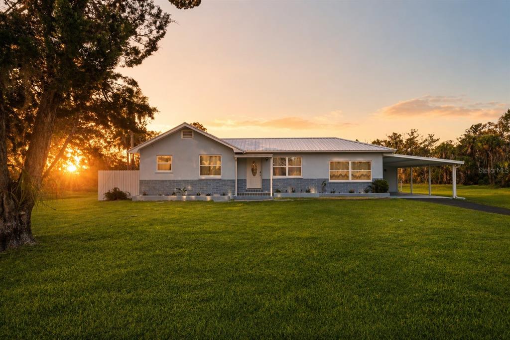 A single-story house with a metal roof, light blue siding, and a carport at sunset — 10928 W FORT ISLAND TRAIL, CRYSTAL RIVER, FL