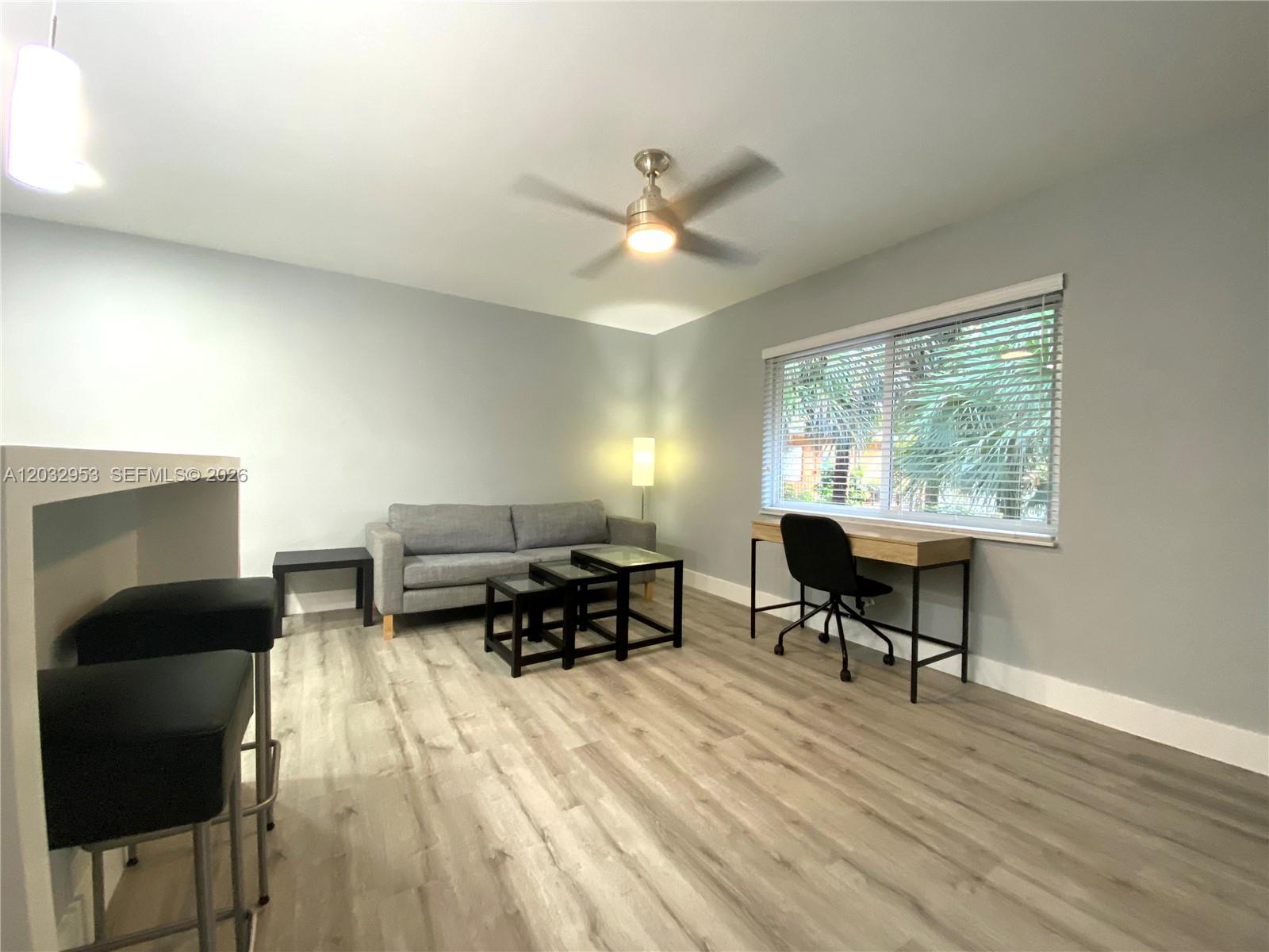 A living room features light wood-look flooring, a gray sofa, a desk, and a ceiling fan — 7901 SW 64 AVE # 18, South Miami FL 33143, SOUTH MIAMI, FL