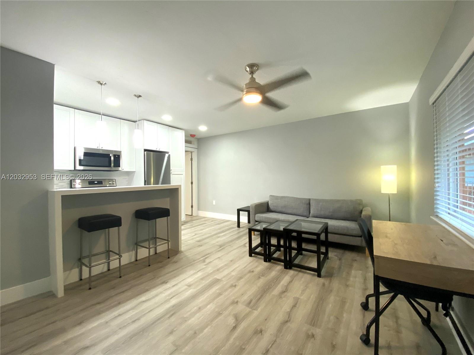An open-concept living area features a kitchen with bar seating, a sofa, and light flooring — 7901 SW 64 AVE # 18, South Miami FL 33143, SOUTH MIAMI, FL