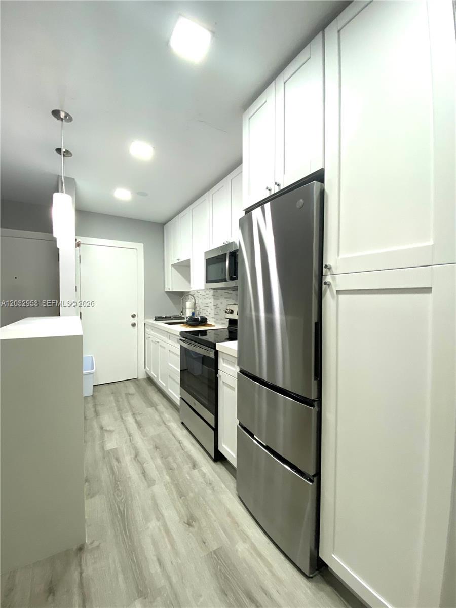 A narrow kitchen features white cabinetry, stainless steel appliances, and light wood-look flooring — 7901 SW 64 AVE # 18, South Miami FL 33143, SOUTH MIAMI, FL