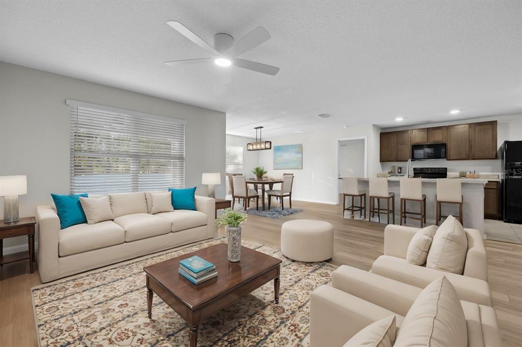 An open-concept living room and kitchen featuring light wood floors, neutral furniture, and a ceiling fan — 896 NW 253RD DRIVE, NEWBERRY, FL