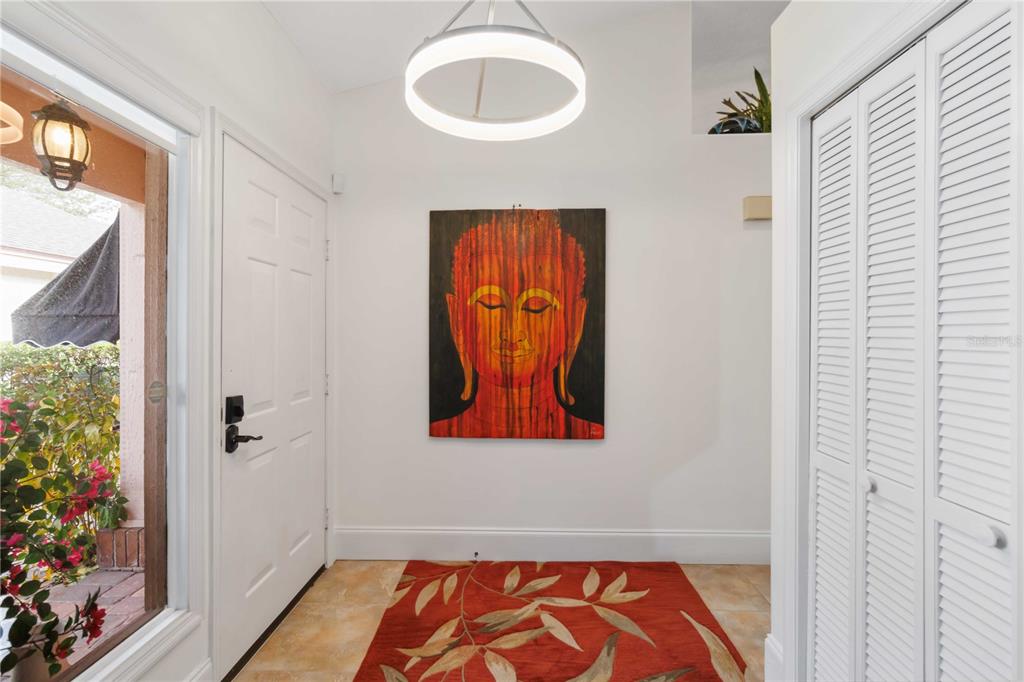 An entryway features a white door, a Buddha painting, a circular light, and tile flooring — 7755 PINE TRACE DRIVE UNIT 7755, SARASOTA, FL