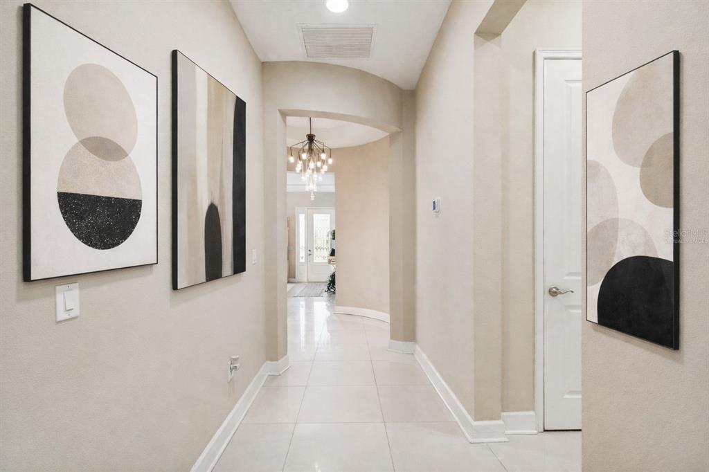 A bright hallway features light tile flooring, neutral walls, and three abstract art pieces — 4155 BARLETTA COURT, WESLEY CHAPEL, FL